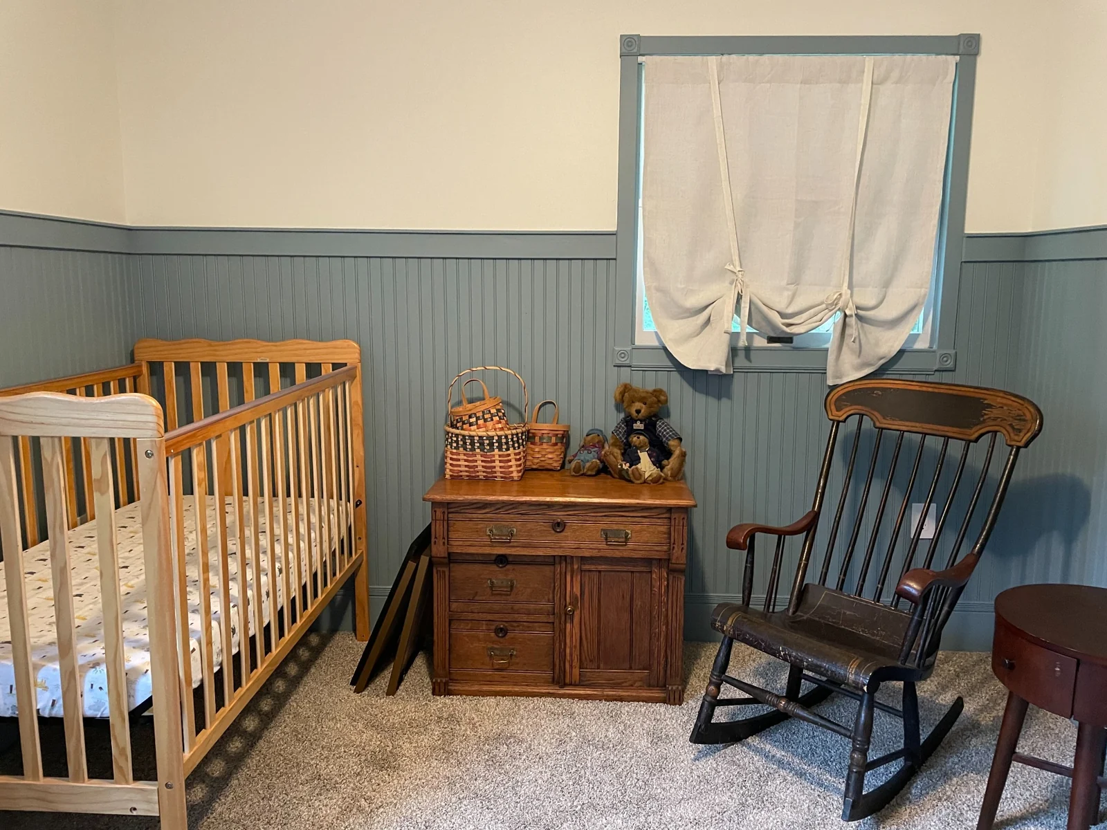 Finished nursery with blue-gray beadboard, antique wood furnishings, and a window framed by decorative trim